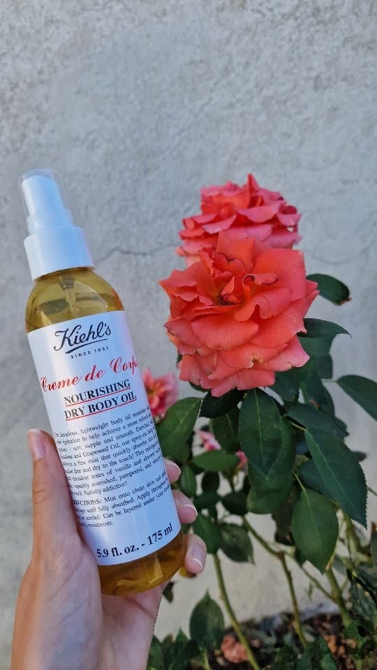 Huile sèche Crème de Corps de Kiehl’s tenue devant des roses