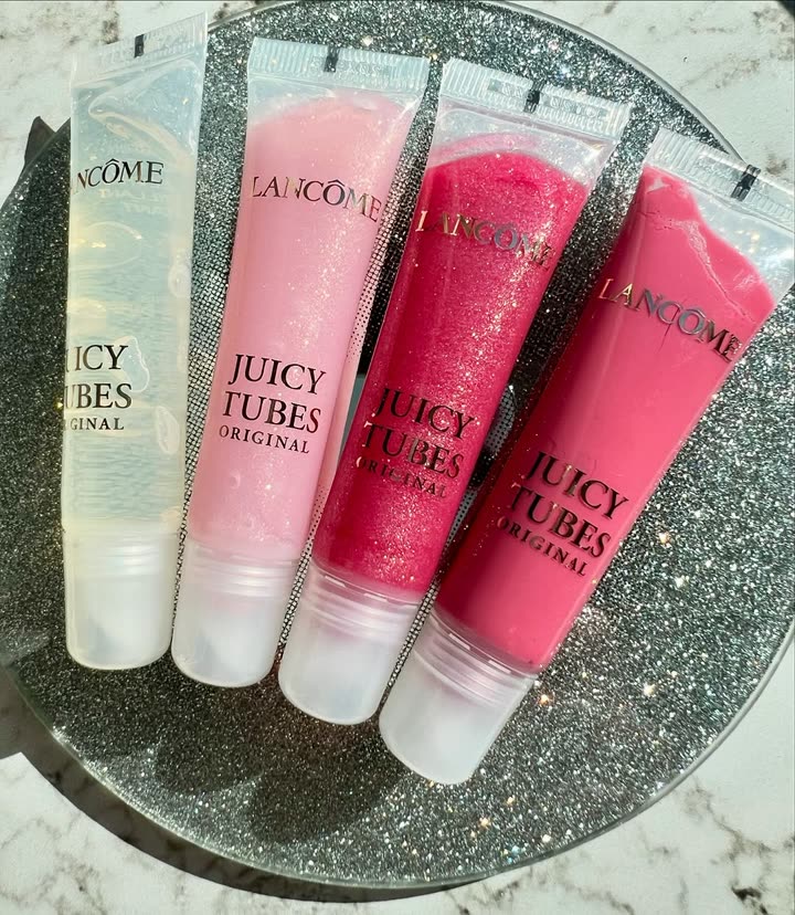 Quatre gloss Juicy Tubes de Lancôme posés sur un plateau pailleté